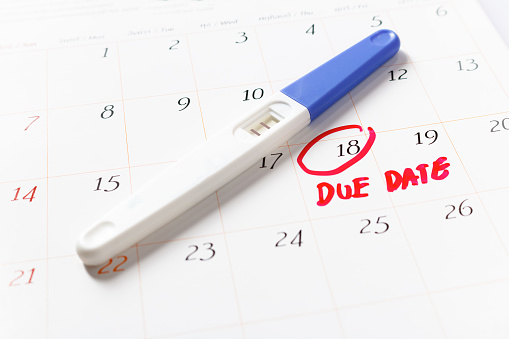 Pregnancy test with positive result lying on calendar; Due Date day; the 18th; Red circled on a white calendar; soft focus.