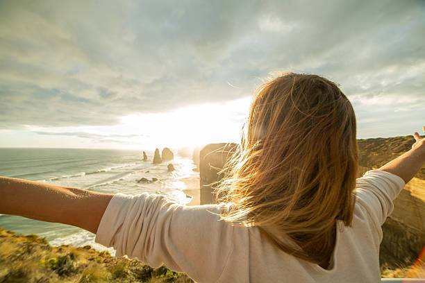Caucasian female arms outstretched at sunset Cheering young woman arms outstretched at sunset. Shot at the Twelve Apostles sea rocks on the Great Ocean Road in Victoria's state of Australia. great ocean road photos stock pictures, royalty-free photos & images