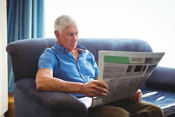 istock Senior man seated on a sofa reading 614035244
