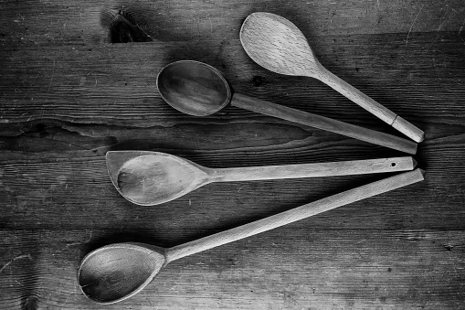 Landscape black and white photograph of a spray of four different wooden spoons against a wood grain background