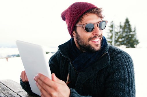 Handsome smiling man in winter outerwear using tablet in the snow