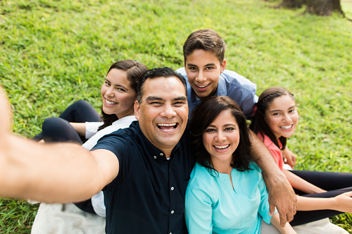 A happy latin family of five taking a selfie and smiling in a horizontal medium shot outdoors.