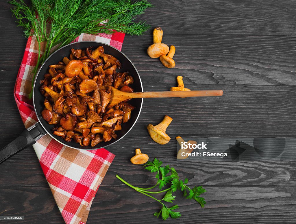 Chanterelle mushrooms fried Chanterelle mushrooms fried in cast iron frying pan, herbs for roasted chanterelles parsley, dill, cloth. Raw chanterelles on a dark brown background of wooden table. Top view. Antipasto Stock Photo