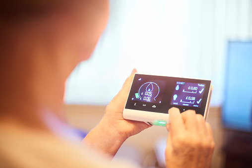 Close up of home owner checking energy consumption on smart meter home technology. They can see their energy consumption and billing all in one place and live costs. Graphics and all identifying have been altered.