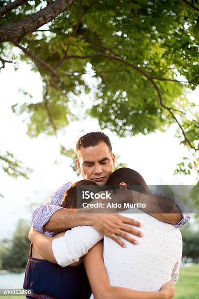 Latin Father Praying With Teen Daughters Under Tree Stock Photo - Download Image Now