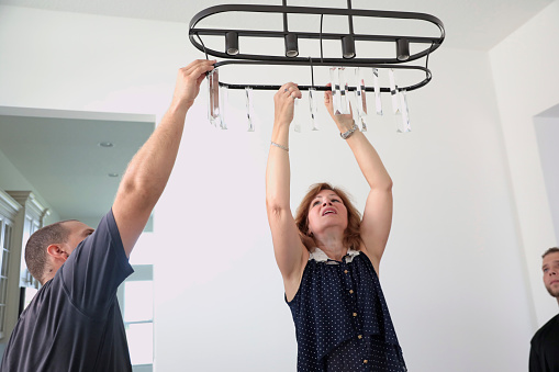 Real Situation. A caucasian female professional stager is hanging a contemporary light fixture in a home for sale Two workers are helping her. Taken with Canon 5D Mark IV.