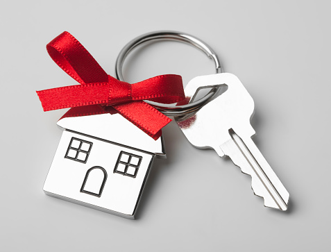 House keys with house shaped keychain with red ribbon on light grey background