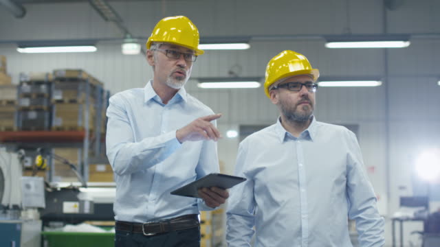 Two employees are walking with tablet computer at logistics center warehouse.