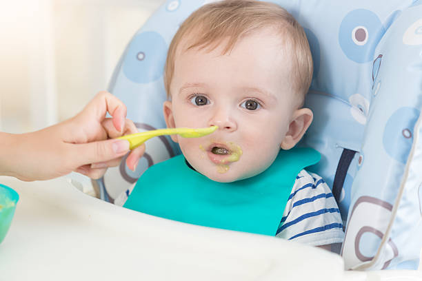 istock Adorable baby in apron eating fruit sauce from spoon 614114064