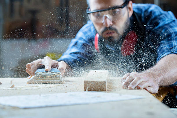 Young handosme carpenter blowing off sawdust Workshop. Shallow DOF. Developed from RAW; retouched with special care and attention; Small amount of grain added for best final impression. 16 bit Adobe RGB color profile. sand paper stock pictures, royalty-free photos & images