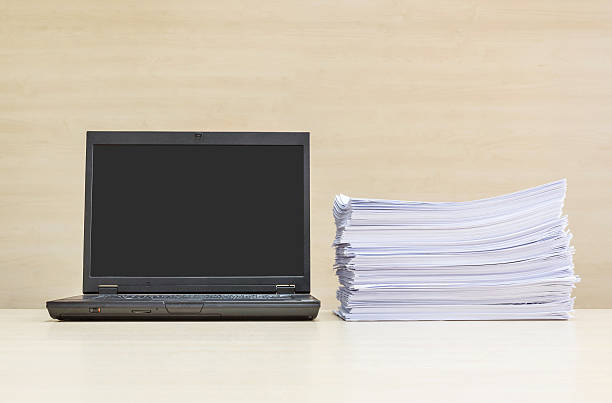 istock Closeup black computer notebook and pile of  paperwork 614128338