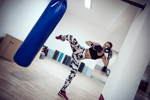 Female Kickboxer Fighter Training and kicking the Punching Bag In the Gym.