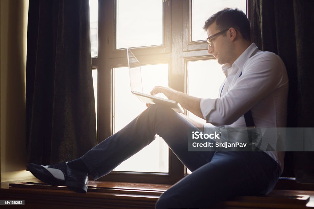 Handsome nerd Young, handsome man with glasses sitting by the window and working on his laptop Luxury Stock Photo