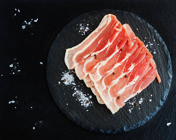 tocino en rodajas crudas sobre fondo de piedra negra. vista superior. - smoked bacon fotografías e imágenes de stock