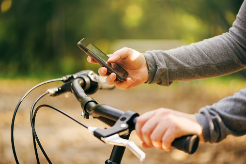 Woman typing text message during bicycle ride, female hands with bicycle using mobile phone outdoors during autumn season, lifestyle and technology concept, selective focus