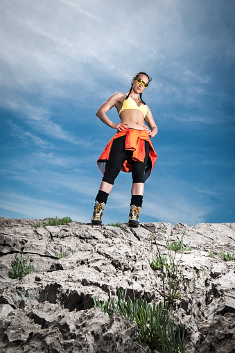 Portrait of female hiker with sunglasses standing on the rocks in the mountain. Sky is behind her.