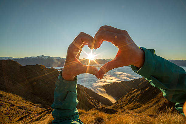 istock Woman frames sun into heart shape, mountain top 614146052