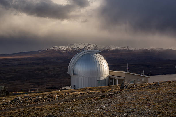 Spectacular view from Mt John observatory. Research telescopes on the foreground and Southern snowcapped Alps on the background. Dramatic stormy sky.