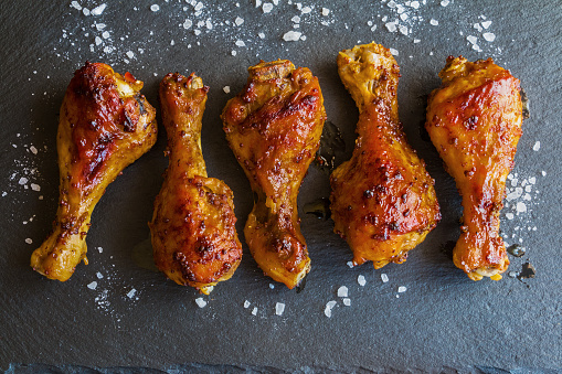 Roasted chicken drumsticks on black background. Cooked with sauce from mustard and olive oil. Top view.