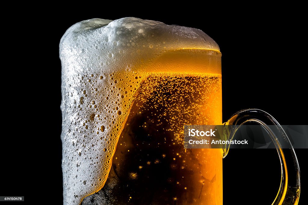 Beer overflowing large glass with foam and bubbles isolated Beer overflowing large glass with foam and bubbles isolated on a black background Beer - Alcohol Stock Photo