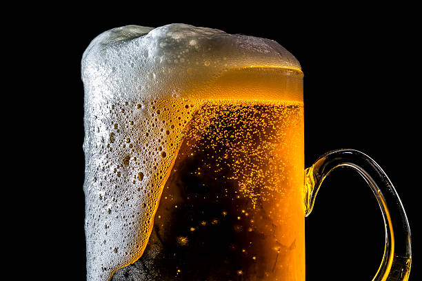 Beer overflowing large glass with foam and bubbles isolated Beer overflowing large glass with foam and bubbles isolated on a black background amber black photography stock pictures, royalty-free photos & images
