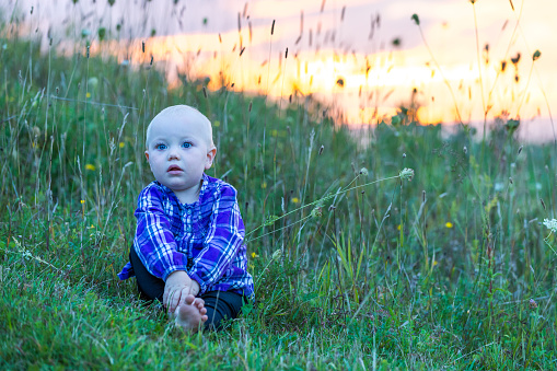 Cute baby seated on a grassy land while gazing at the surroundings.