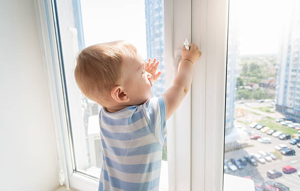 Baby in danger. Baby boy pulling handle of window