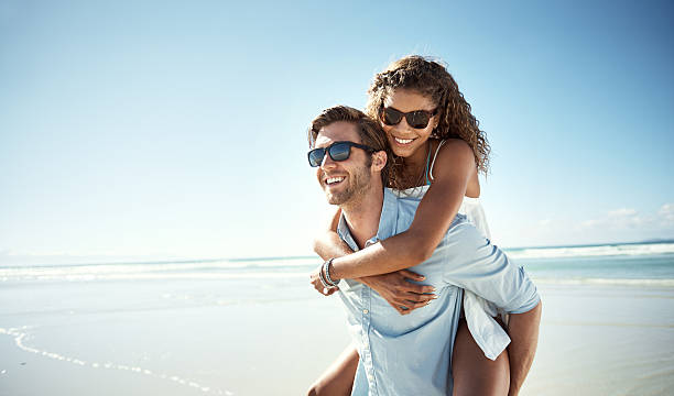 What a beautiful place to be in love Shot of a young man piggybacking his girlfriend on the beach arm around photos stock pictures, royalty-free photos & images