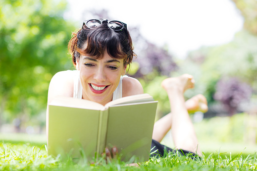 young woman lying down reading a book in a park