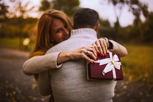 Man and woman hugging in the park,after a man gave his beautiful wife a present