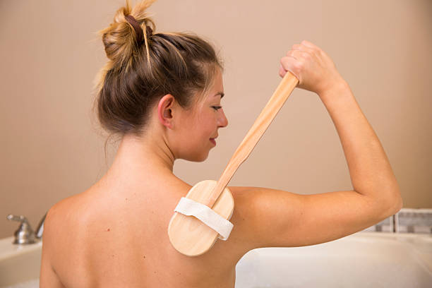 Dry Brushing Back of Shoulder 2 Bare back of young woman in tub holding handled dry brush to back of her shoulder back brush stock pictures, royalty-free photos & images