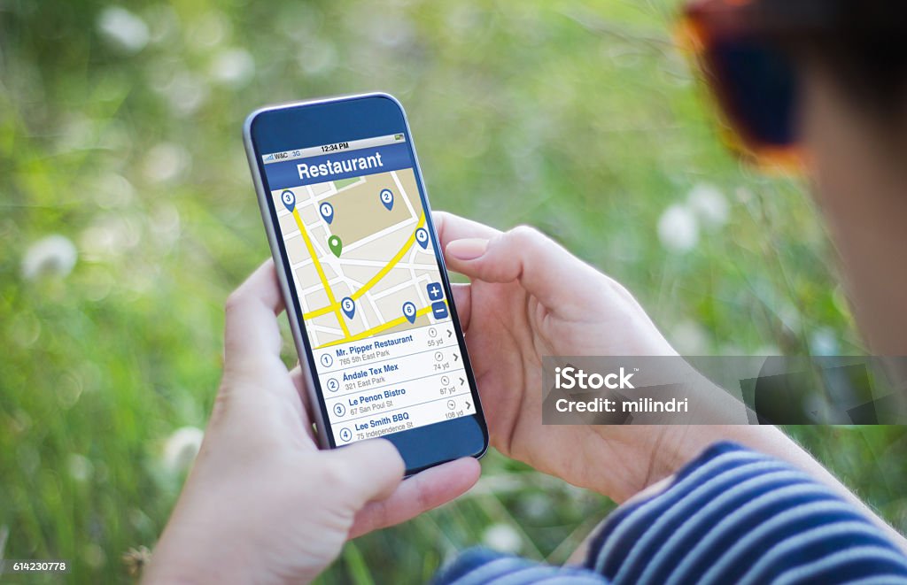 girl in grass holding her smartphone restaurant search woman sitting on the grass looking for a restaurant with her smartphone. All screen graphics are made up. Telephone Directory Stock Photo