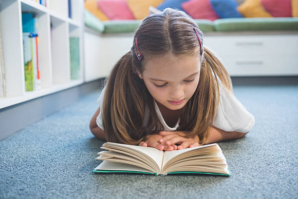 istock Schoolgirl lying on floor and reading a book in library 614231930
