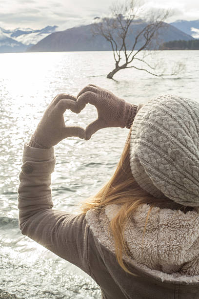 istock Young woman makes heart shape finger frame on lake Wanaka 614234710