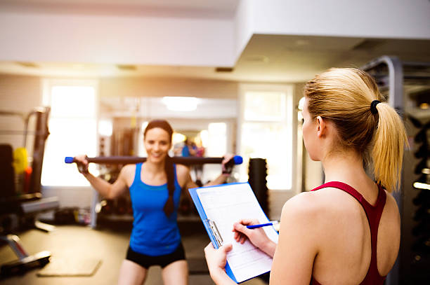 istock Woman exercising in gym, personal trainer, plan on clipboard 614237526
