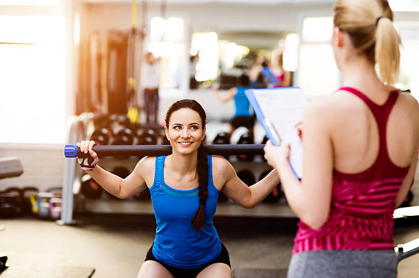 istock Woman exercising in gym, personal trainer, plan on clipboard 614238584