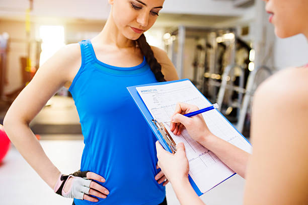 istock Woman with personal trainer in gym, plan on clipboard 614239296
