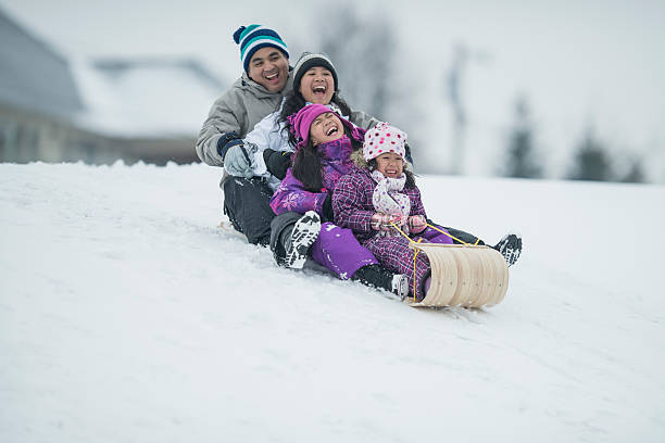Sledding A multi-ethnic family is having fun in the snow on a winter day. Here, they are sledding down a hill in their toboggan. snowing photos stock pictures, royalty-free photos & images