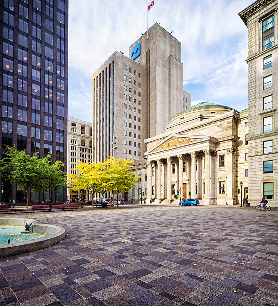 Old Montreal place d'armes with bank buildings Montreal, Canada - October 12, 2016: Old Montreal place d'armes featuring the buildings for National bank and Bank of Montreal. A cyclist is passing by, a few cars are parked in the distance. Fall colored trees are visible. place darmes montreal stock pictures, royalty-free photos & images