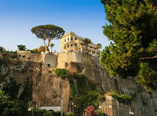 Capri, Italy - September 10, 2008: Gorgeous Villa on a Hill, Capri, Italy. Capri is an island in the Tyrrhenian Sea next to Sorrentine Peninsula, in the Gulf of Naples in the Campania region of Italy. The main town of the island is Capri - which is the same name as the island. It has been a resort since the time of the Roman Republic. Green trees, bushes, rocks, street lamps, flowers and vivid blue clear sky are in the image.