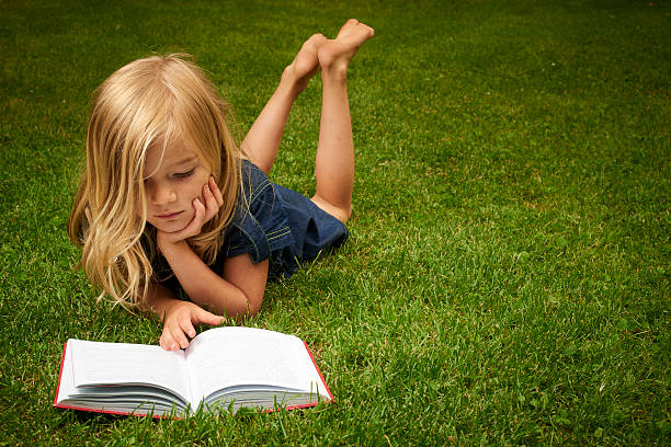 little girl reading a book in the park