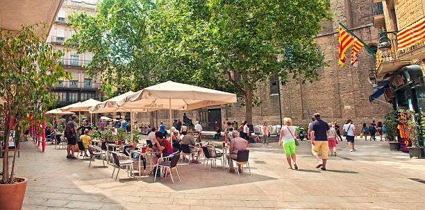 Barcelona, Spain - June 9, 2016: street cafe and people walking around at small square in old part of the city on sunny summer day