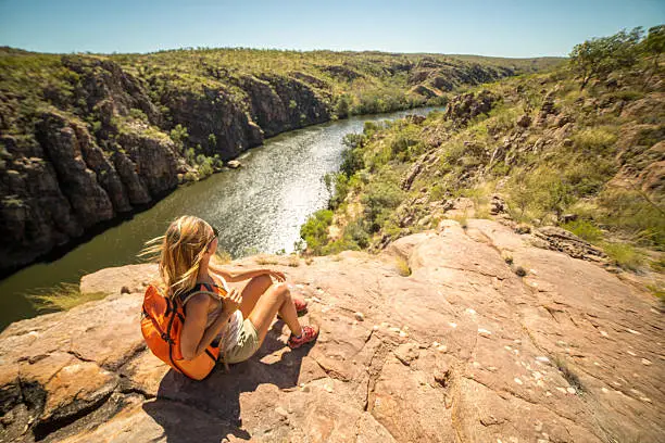 Young woman hiking sits on cliff and looks at view, Katherine Gorges on the background. Beautiful Summer day.