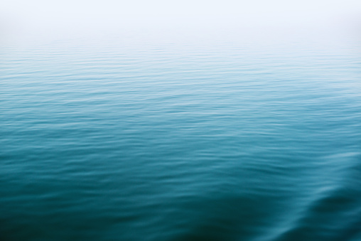 Small ripples and soft waves on the surface of a calm, deep lake. Horizon is hidden in fog.