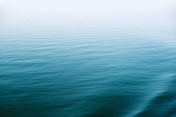 Calm and deep blue lake Small ripples and soft waves on the surface of a calm, deep lake. Horizon is hidden in fog. water surface stock pictures, royalty-free photos & images