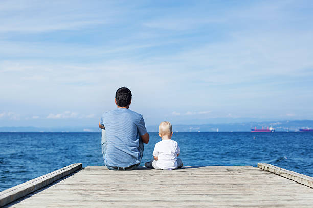 padre con figlio seduto sul molo di mare - lake summer beach nautical vessel foto e immagini stock