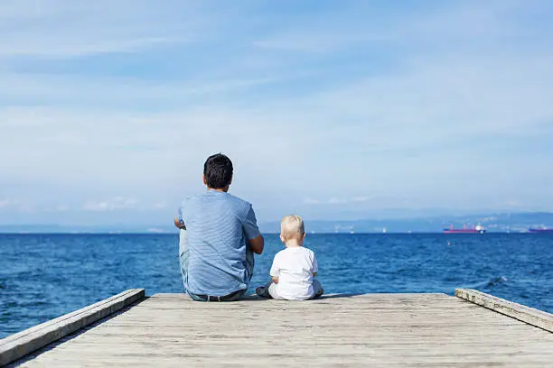 Photo of Father with son sitting on the sea pier