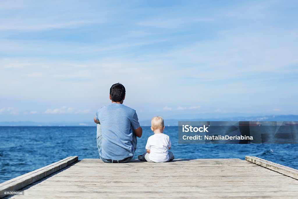 Pai com o filho sentado no cais do mar - Foto de stock de Pai royalty-free