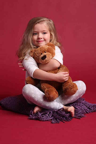 istock Baby in pajamas hugging a bear. Red background 614315254
