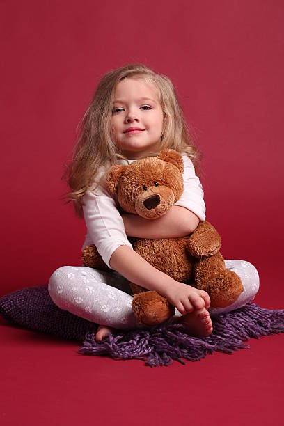 istock Kid in pajamas hugging a bear. Red background 614315272